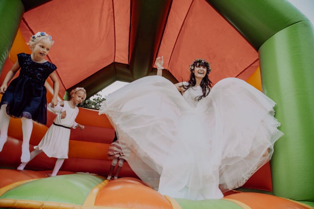 Braut hüpft mit Kindern auf der Hüpfburg